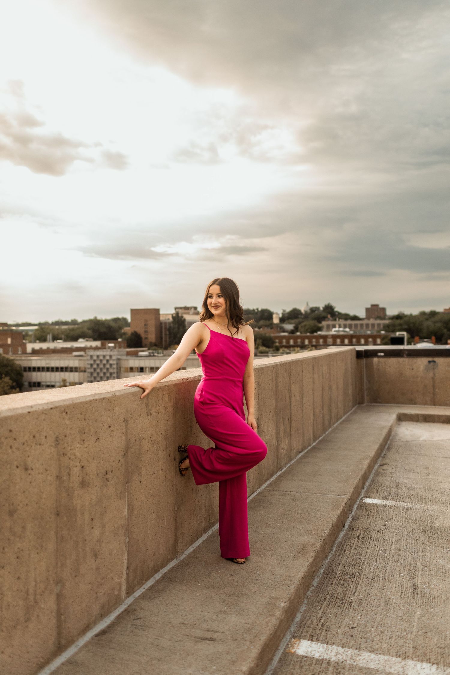 Woman in vibrant red gown poses on urban rooftop during golden hour sunset.