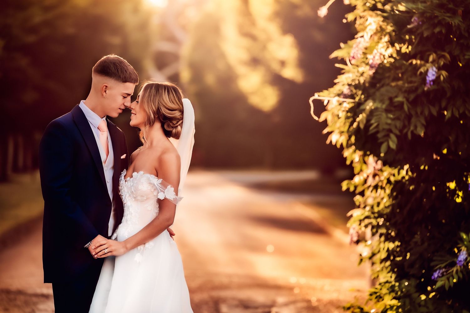 A romantic wedding photo of a couple embracing in golden sunset light among garden foliage.
