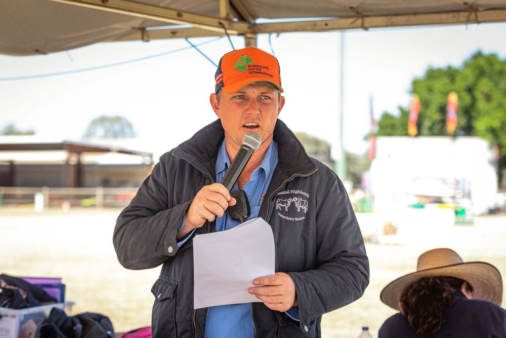Speaker holds microphone under event tent during outdoor gathering.