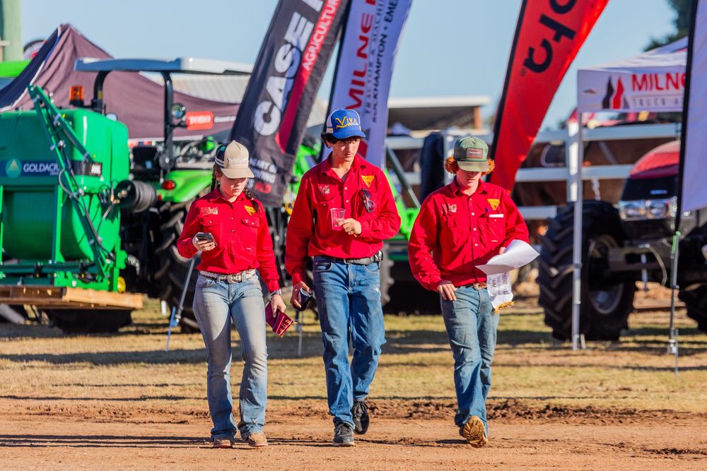 Three people in red shirts walk through an agricultural equipment display area.