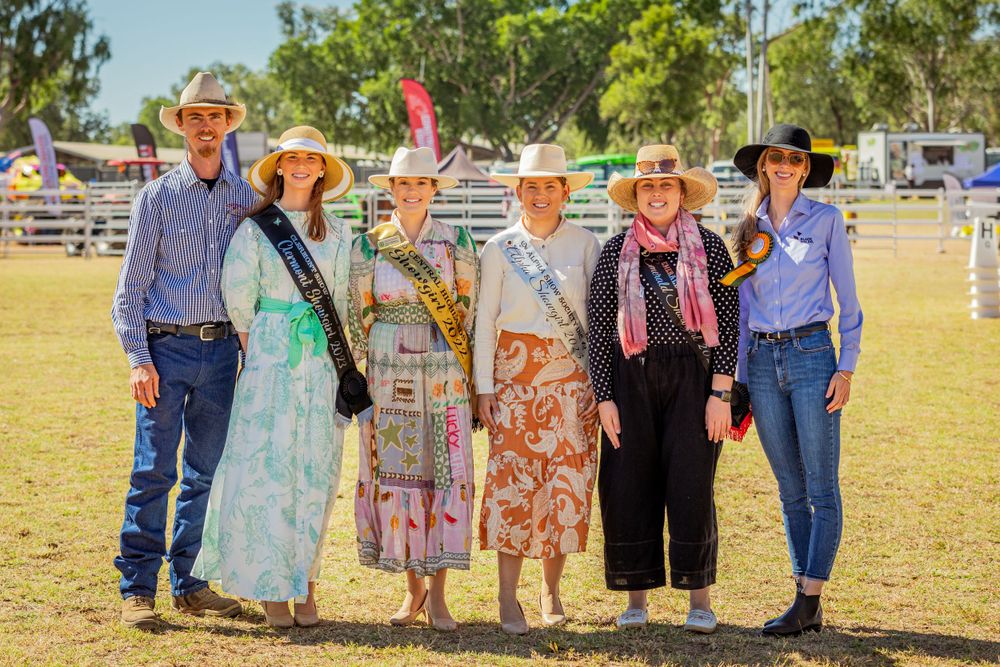 Group of attendees in western wear pose together at outdoor country event.