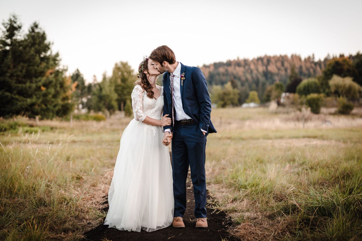 Romantic wedding couple embracing in rustic outdoor field with autumn foliage backdrop.