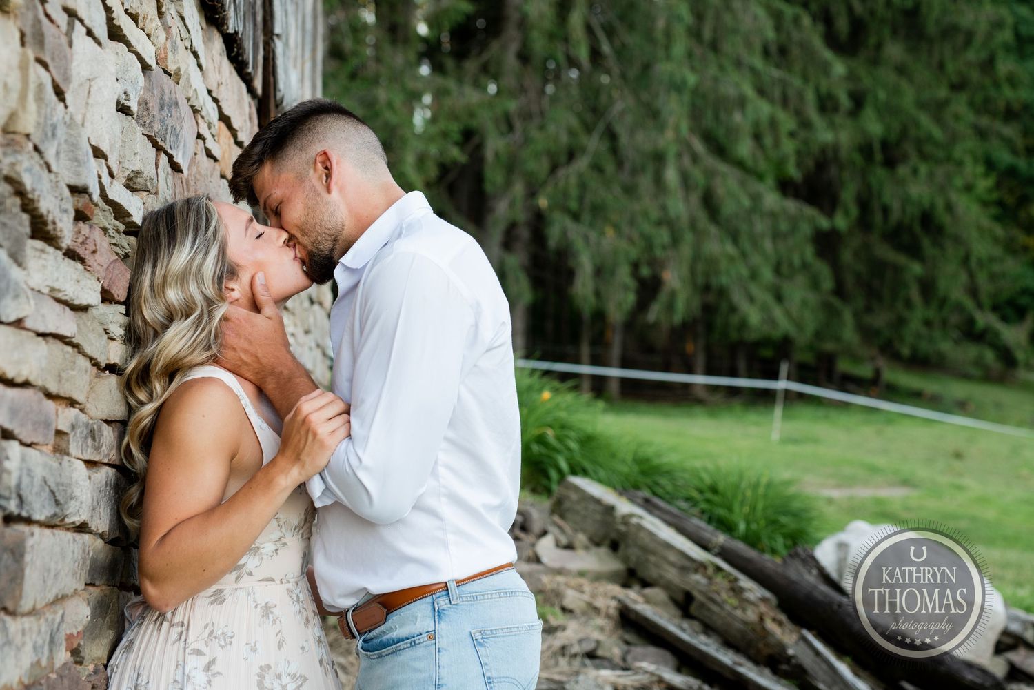 A tender moment shared against a rustic stone wall during an engagement photoshoot.