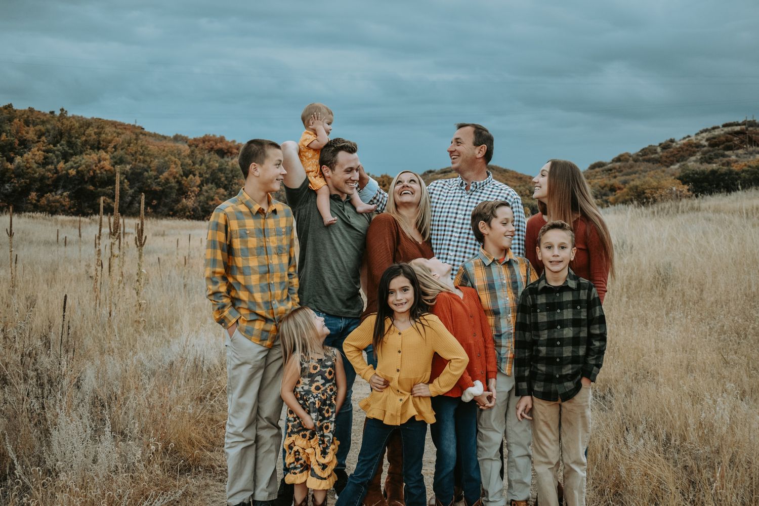 Large family posing together in golden autumn field with dramatic cloudy sky backdrop.
