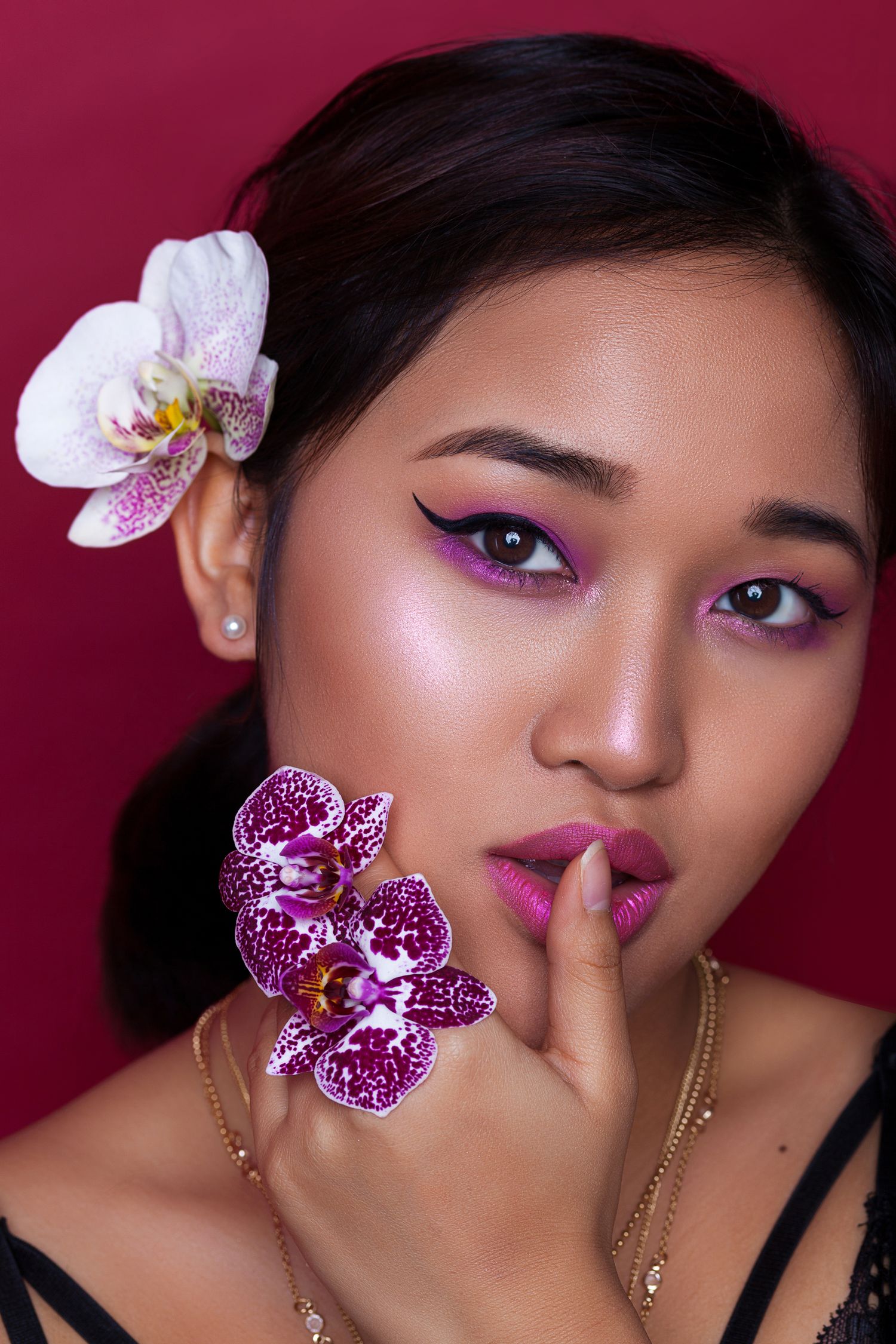 Asian beauty portrait with vibrant pink eye makeup and orchid flowers against burgundy background.