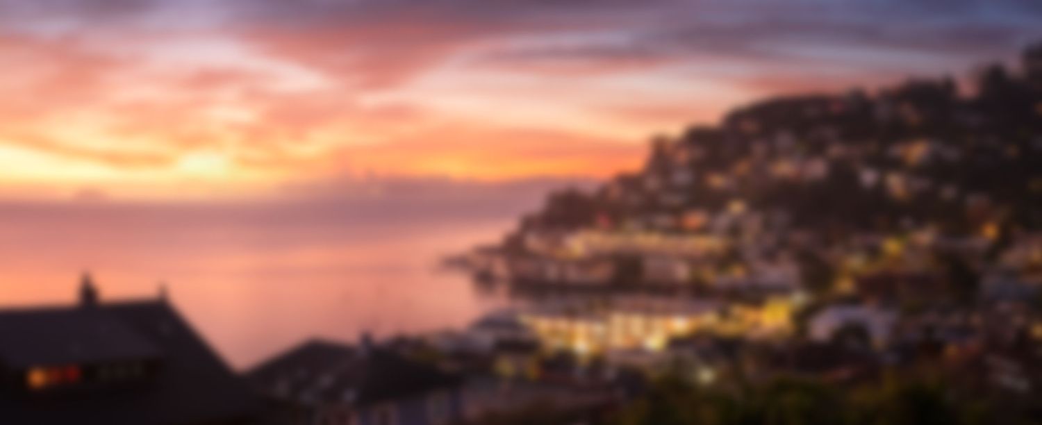 Blurred coastal cityscape at sunset with orange and purple sky.