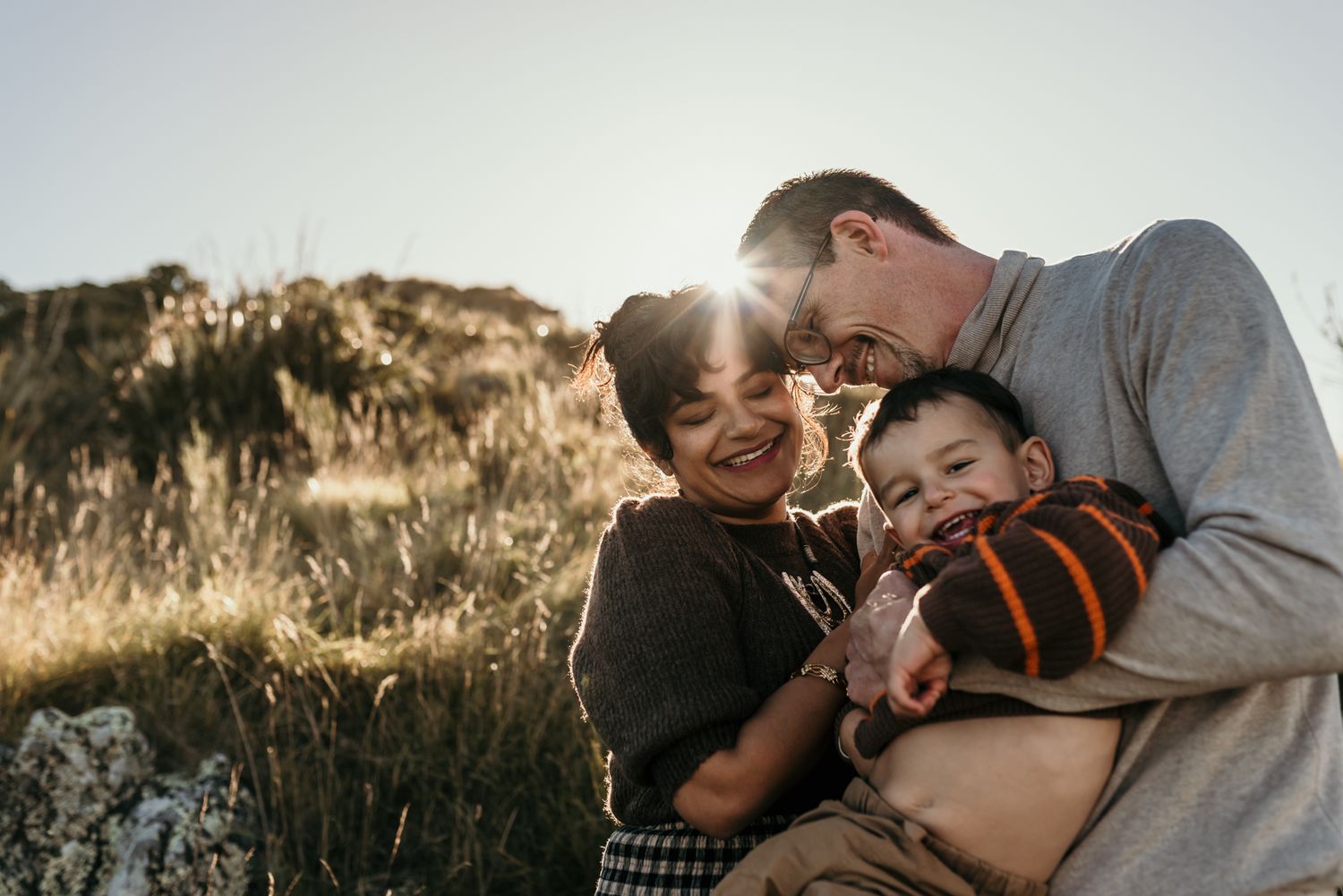 An intimate family moment captured during golden hour on a hillside with joyful expressions and laughter.