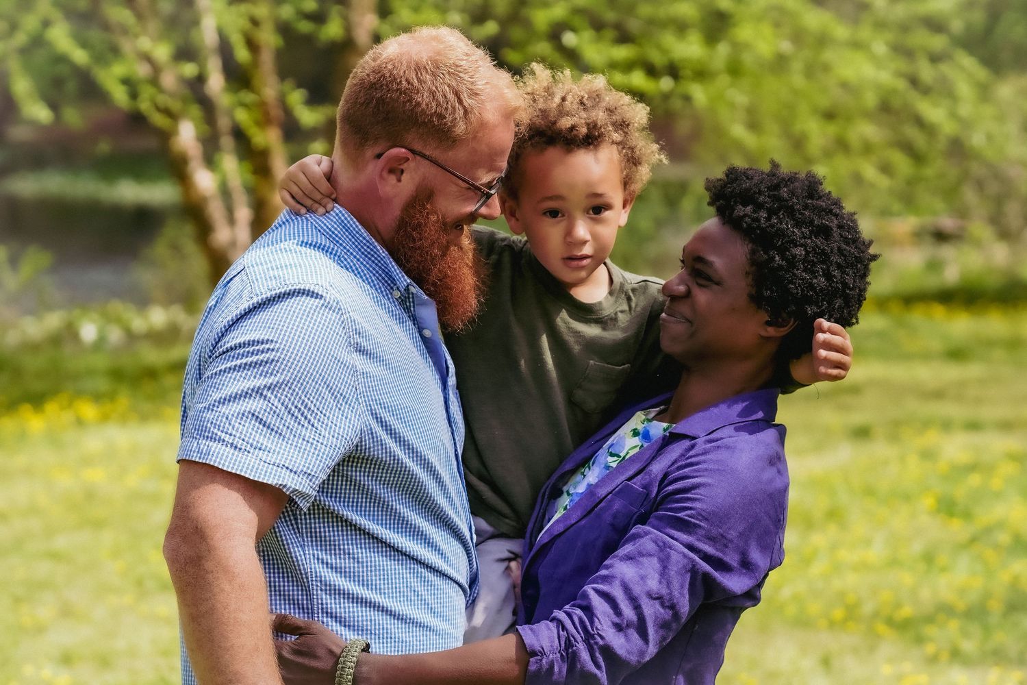 A loving family embrace together outdoors in a sunny park setting.