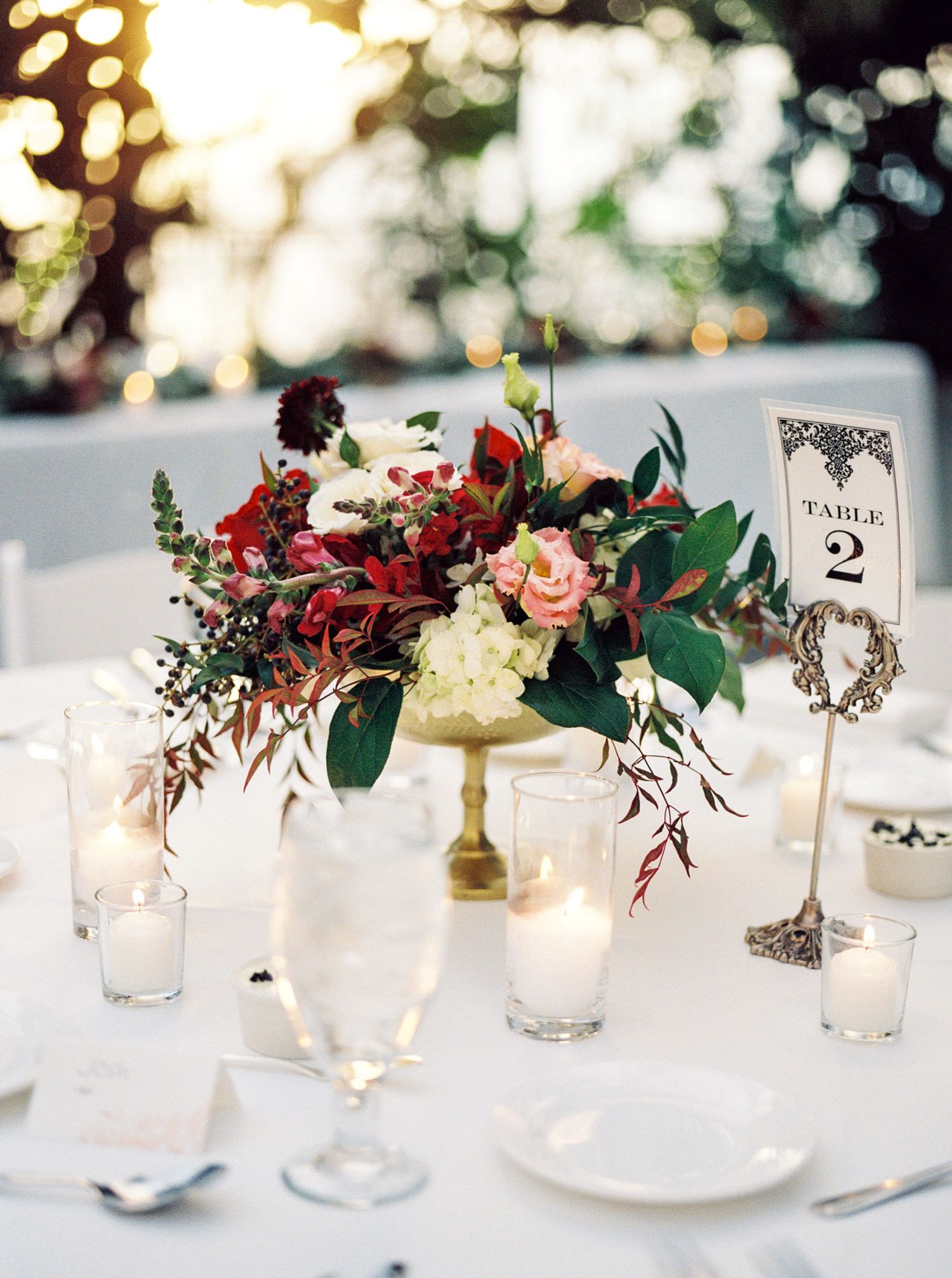 red floral centerpiece on a candlelit table indoors at the la caille greenhouse wedding