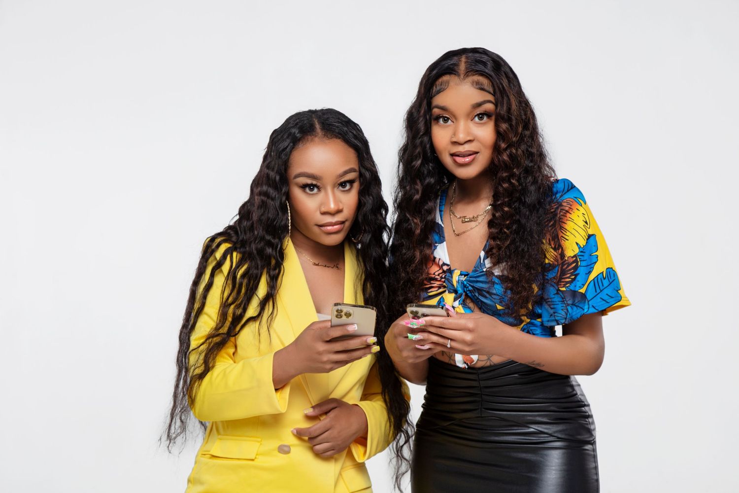 Two friends in yellow and blue outfits sharing drinks and laughing together during a photoshoot.