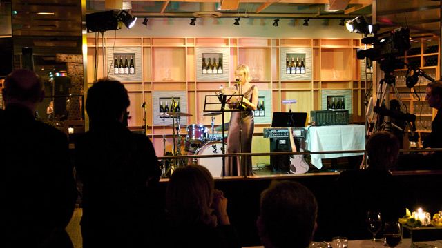 A dimly lit performance venue with audience silhouettes and stage lighting.