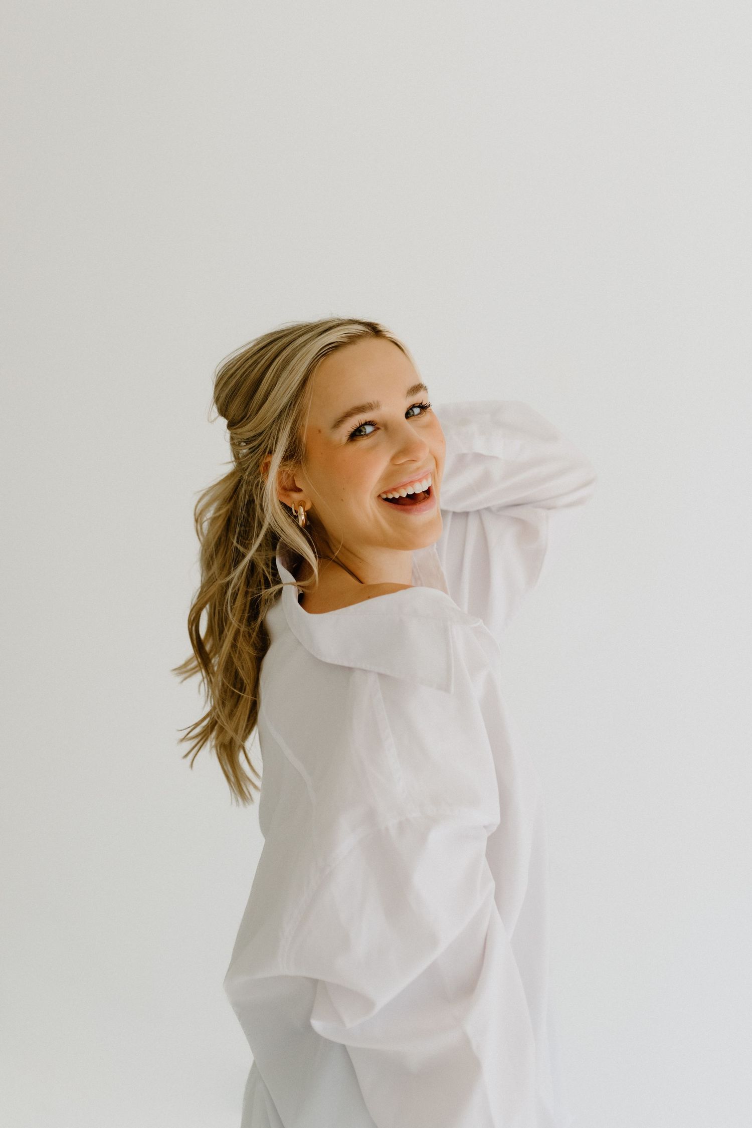 Woman in white blouse laughing joyfully against white background in studio setting.