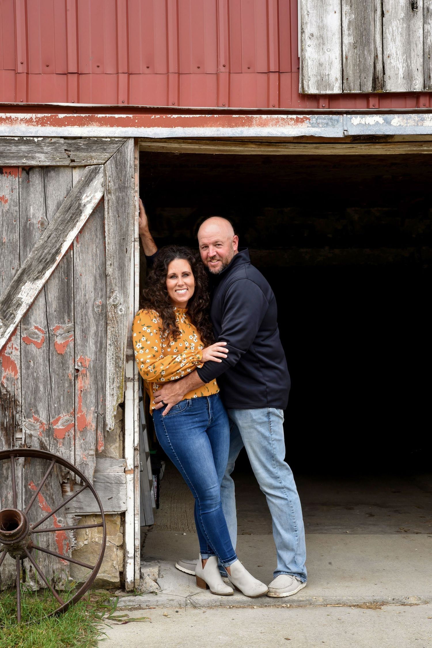 A couple embraces in the doorway of a red barn with rustic wooden details.