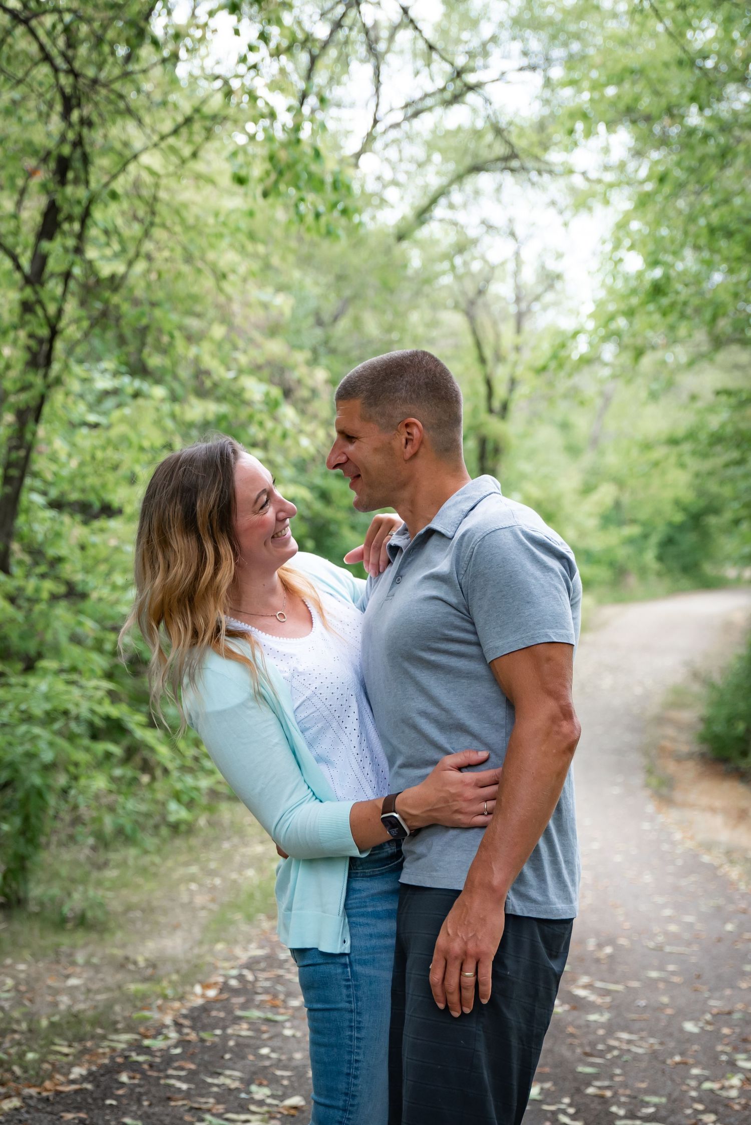 A couple shares an intimate moment while standing on a tree-lined path in a park.