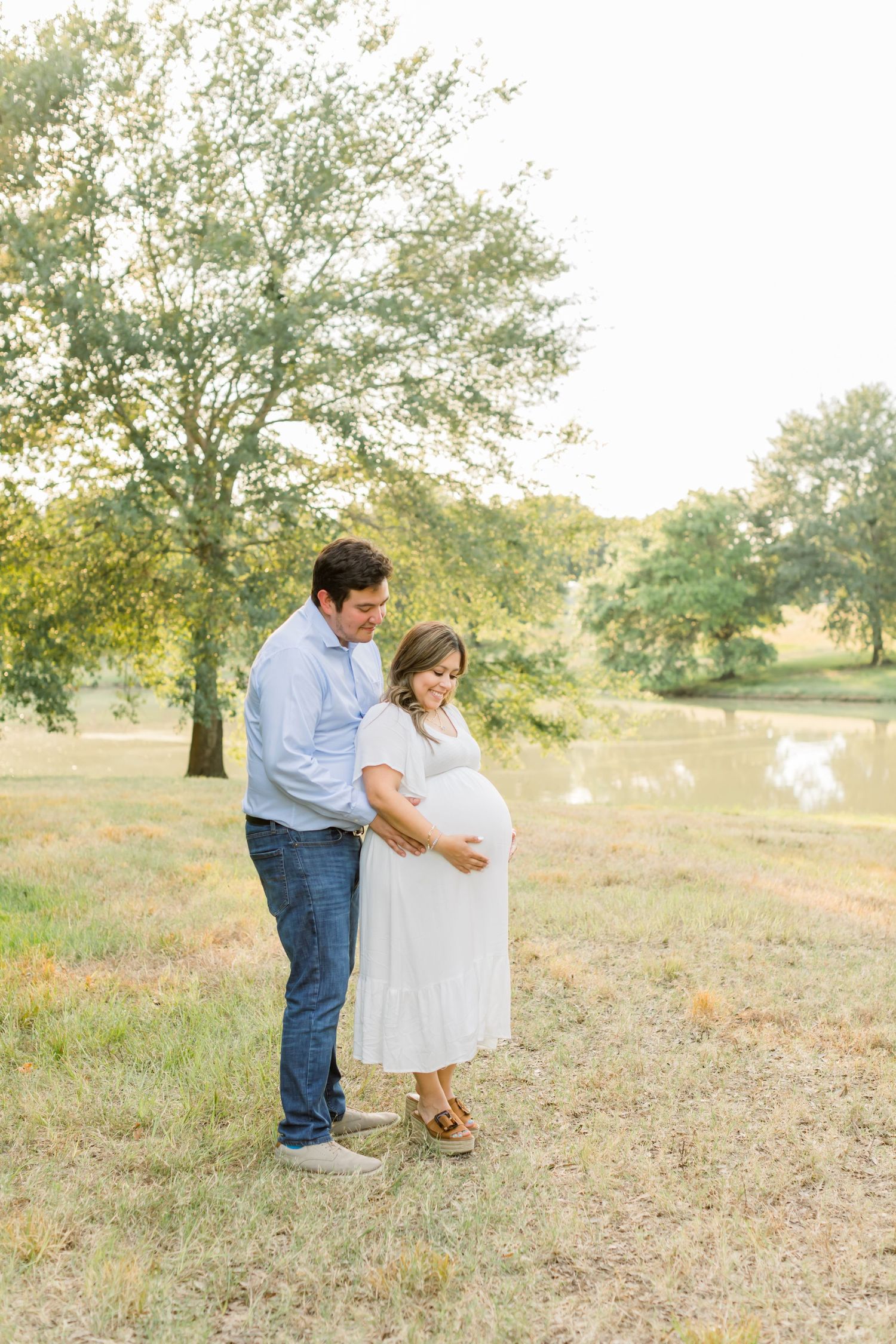 A tender maternity portrait of a couple standing together in golden evening light.