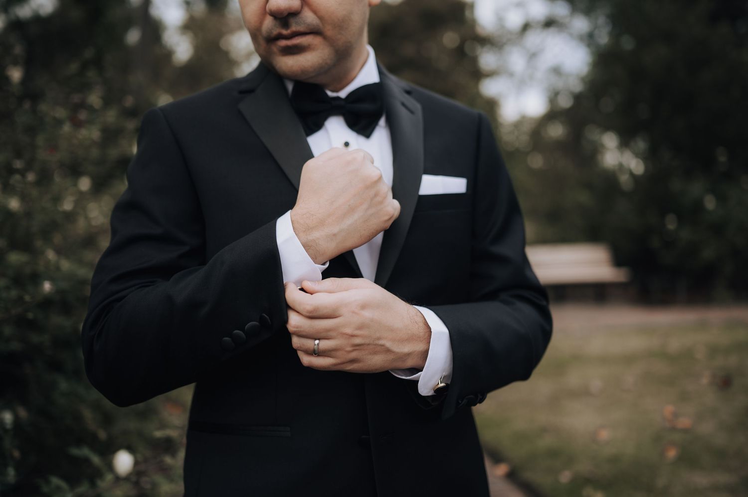 Close-up shot of groom adjusting his bowtie while wearing a classic black tuxedo.