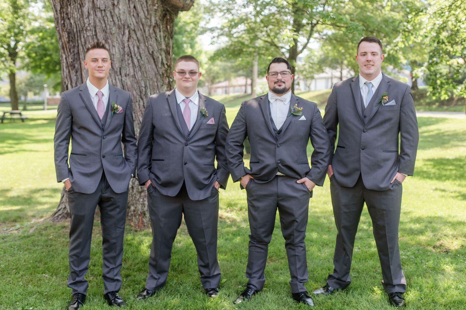 Wedding party in matching grey suits standing together outdoors in a park setting.