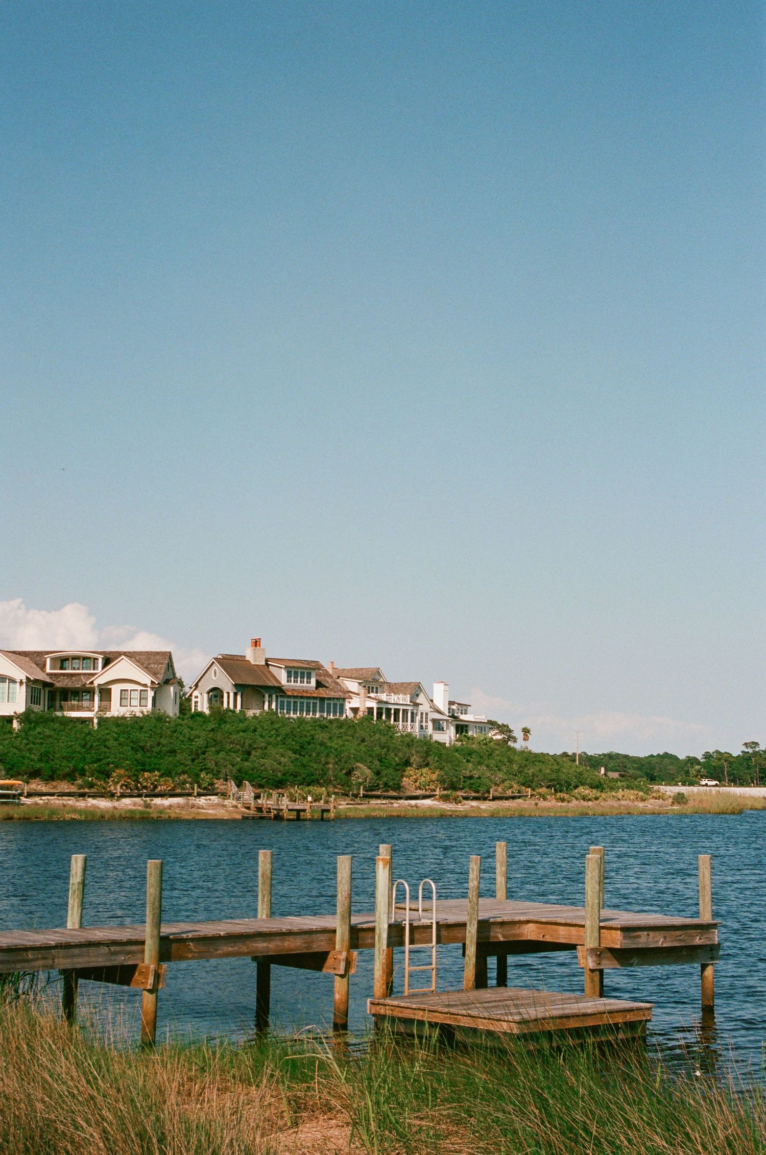 Wooden dock with waterfront houses along the coastline on a sunny day.