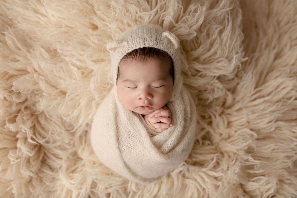 eden prairie newborn photographer | baby-wrapped-in-cream-knitted-wrap-with-knitted-hat-with-bear-ears-on-cream-rug