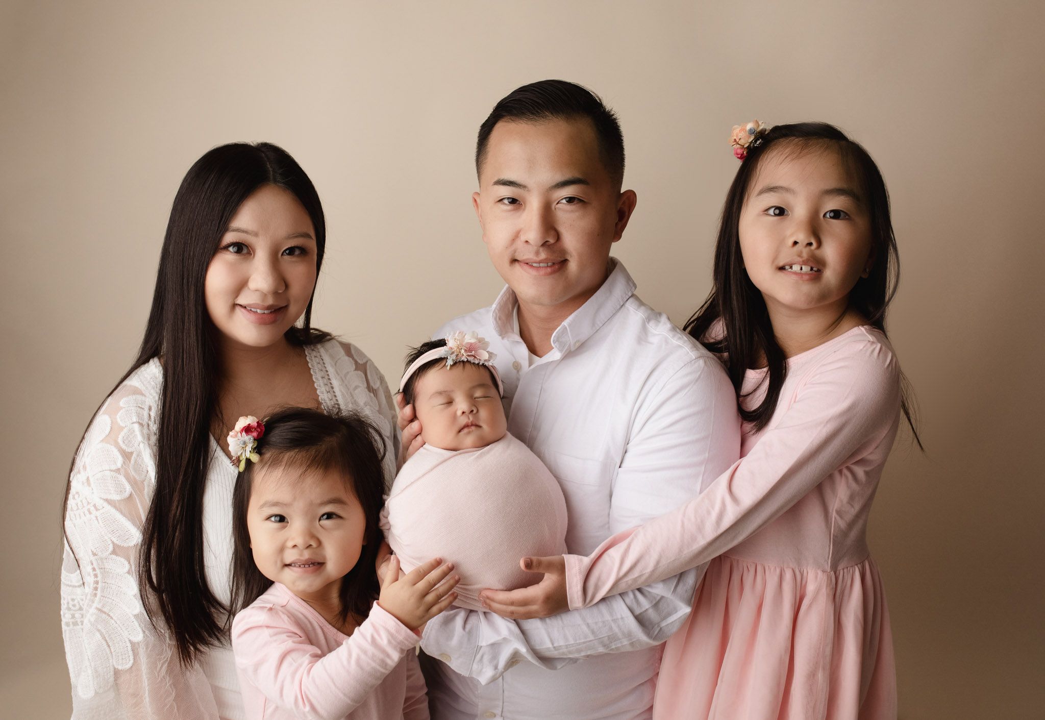 Eden Prairie newborn photographer | Family-of-5-wearing-pink-and-white-holding-newborn-wrapped-pink-wrap-cream-backdrop