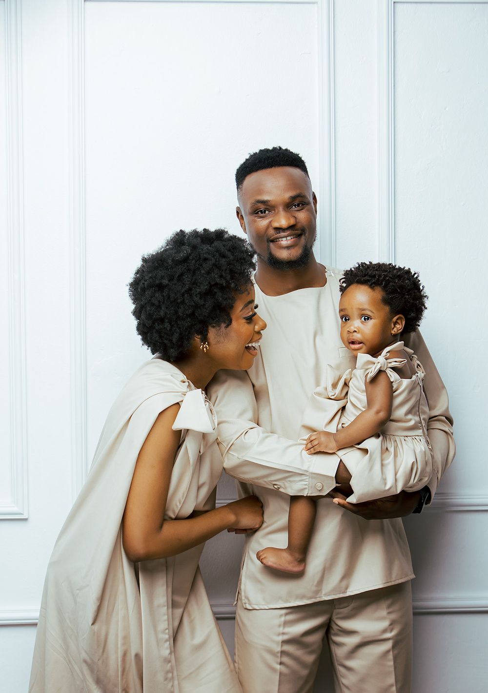 Family in matching beige outfits share a joyful moment against a white wall.