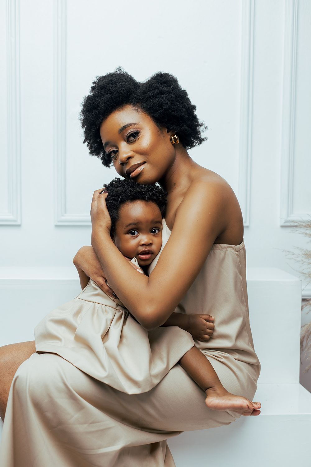 Tender moment between parent and child in matching beige outfits against white backdrop.