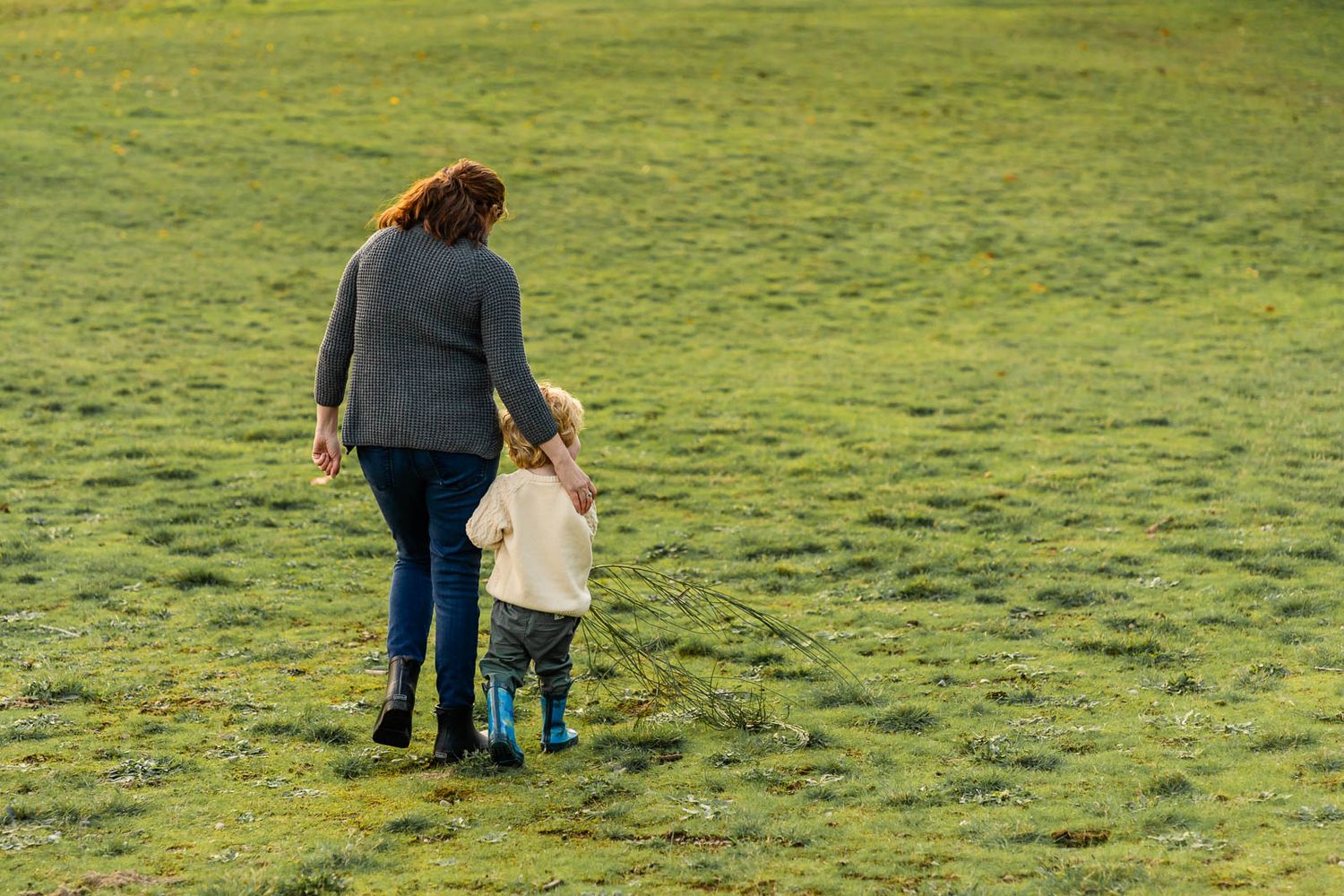Mother and son walking in a grassy field.