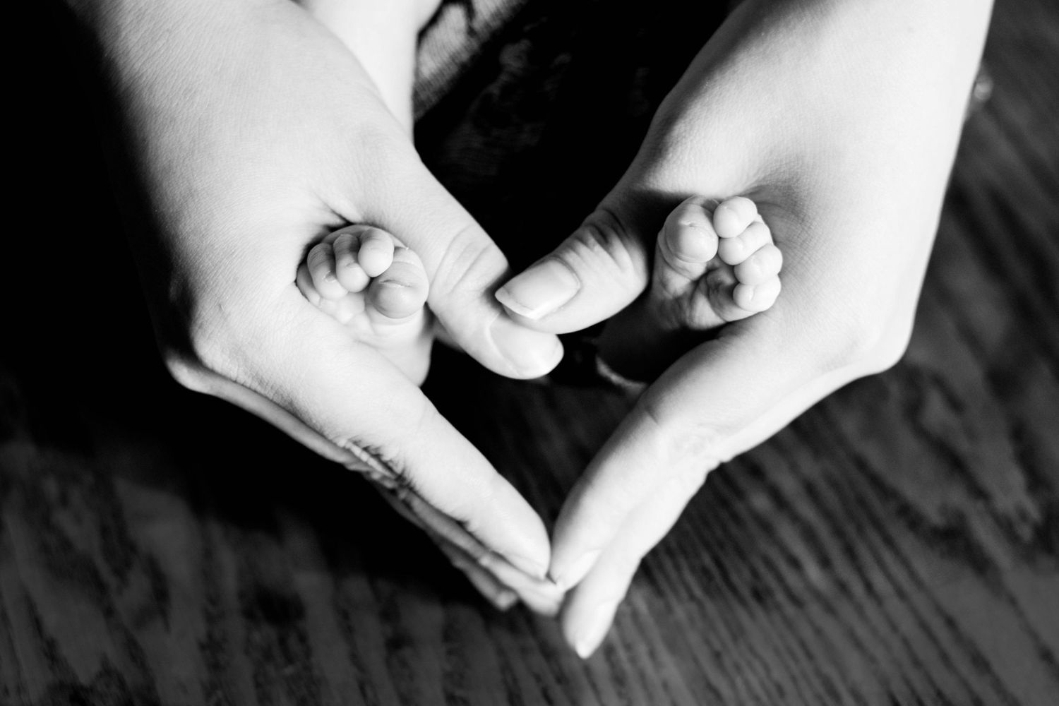 Black and white photo of hands forming a heart shape with baby hand in center.