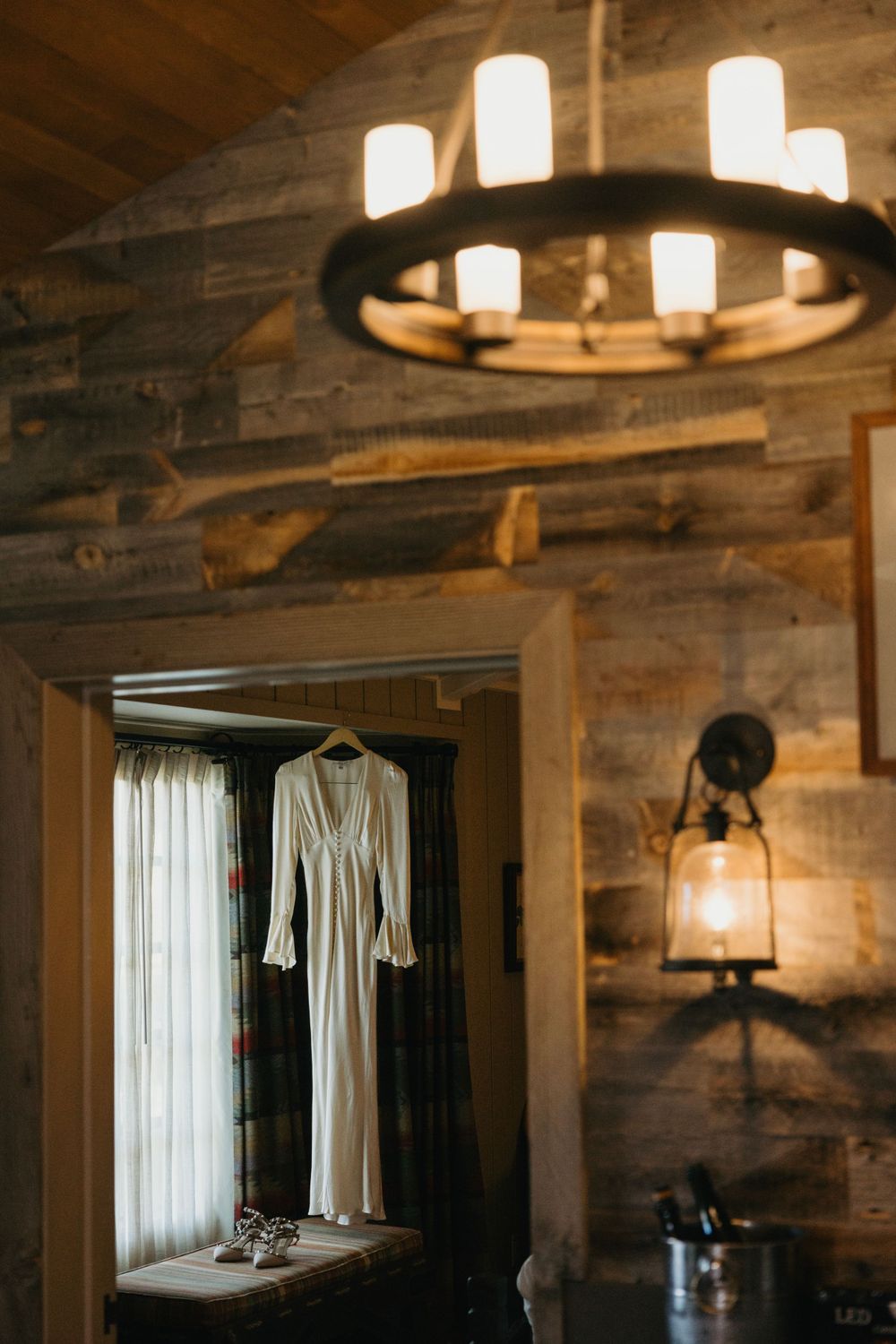 Rustic wooden room with hanging lights and white dress displayed.