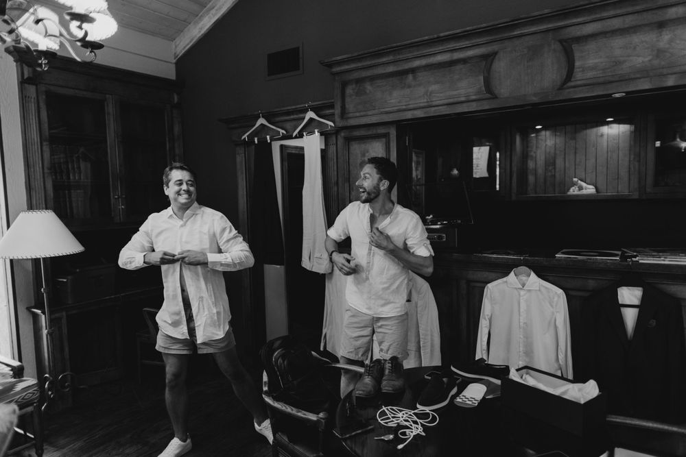 Men in formal attire getting ready in a dimly lit room with wood paneling.