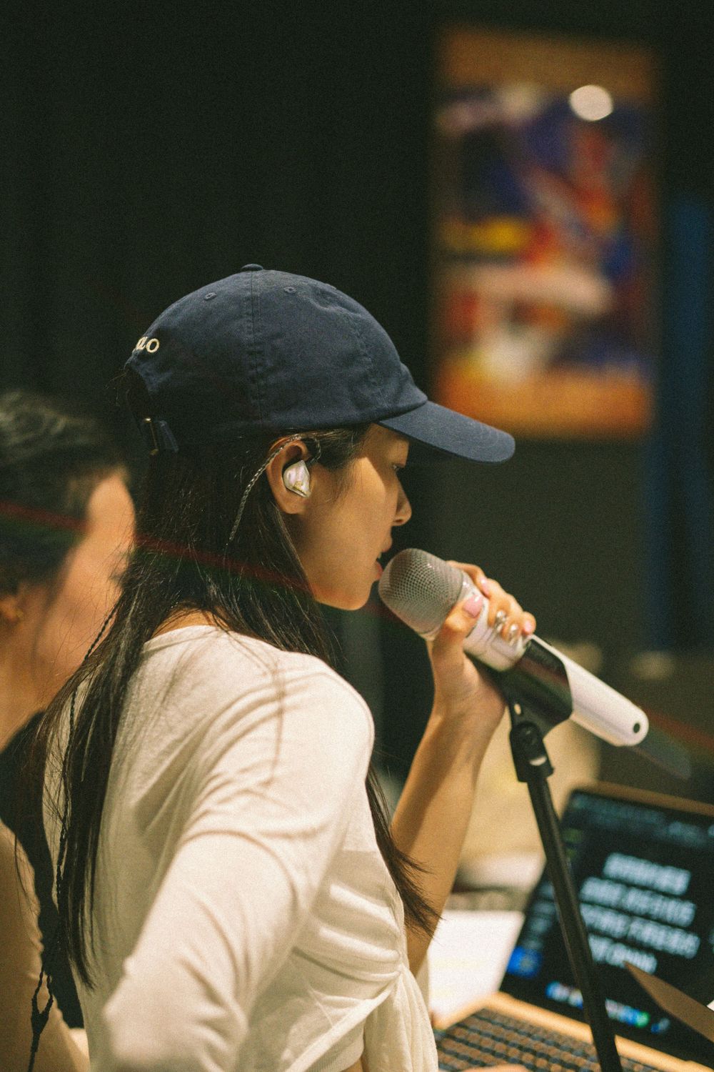 Performer in white shirt and baseball cap sings into microphone during rehearsal.
