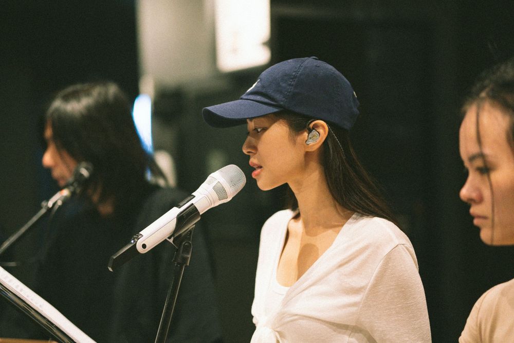 Singer in baseball cap performs with microphone against dark background.