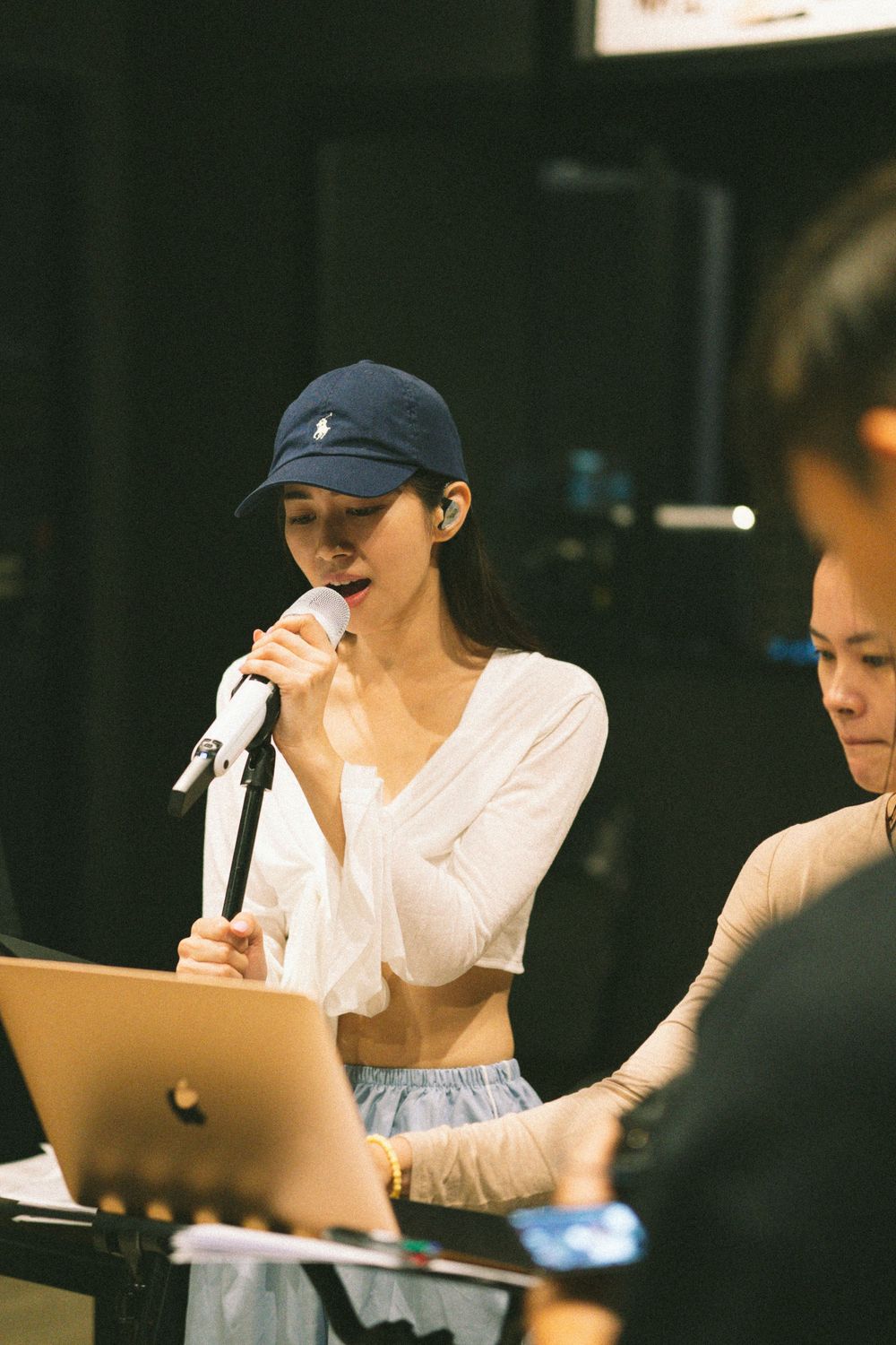 Musician performs with microphone while reading from laptop during rehearsal.