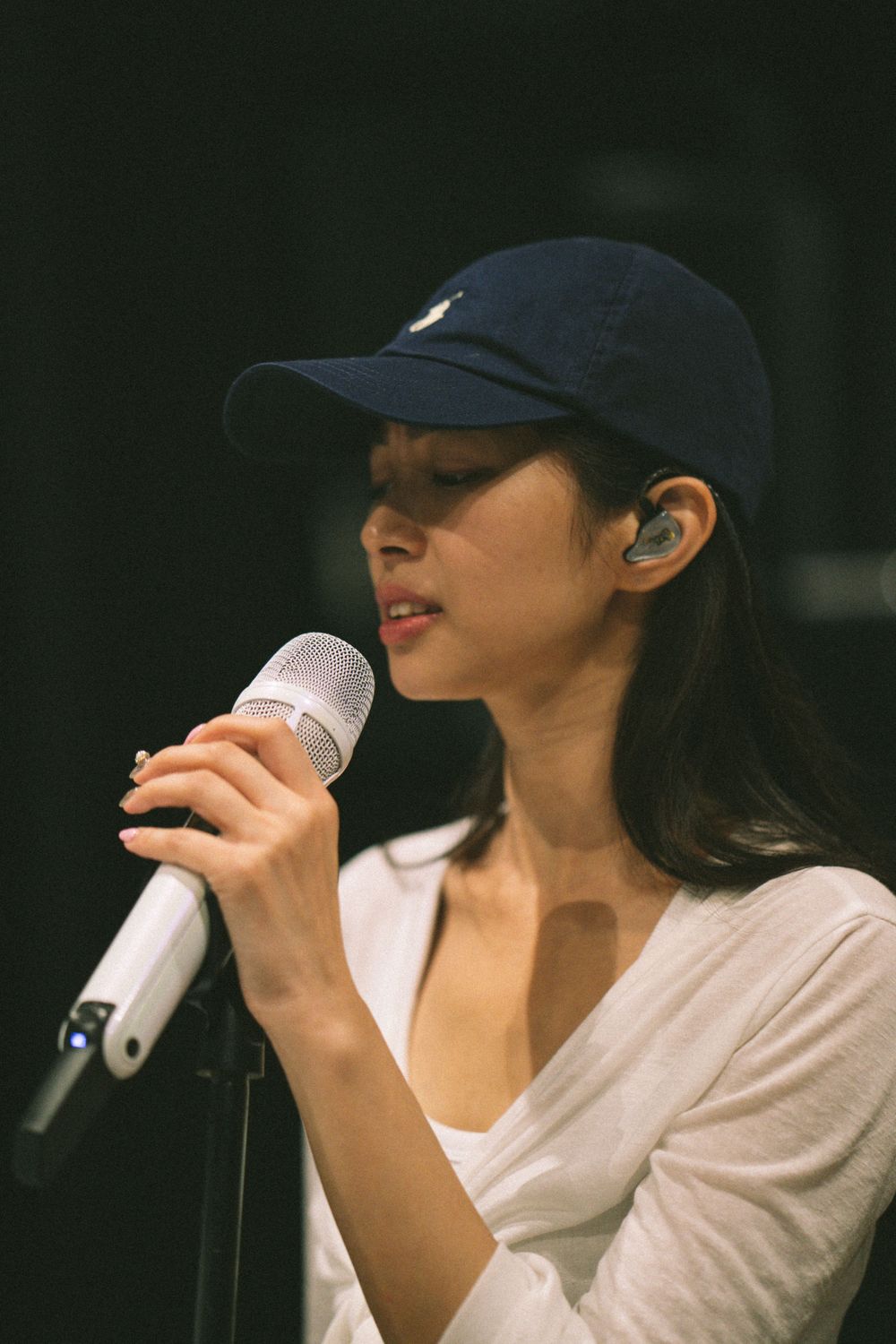 Singer in navy cap and white top performs with microphone during studio session.