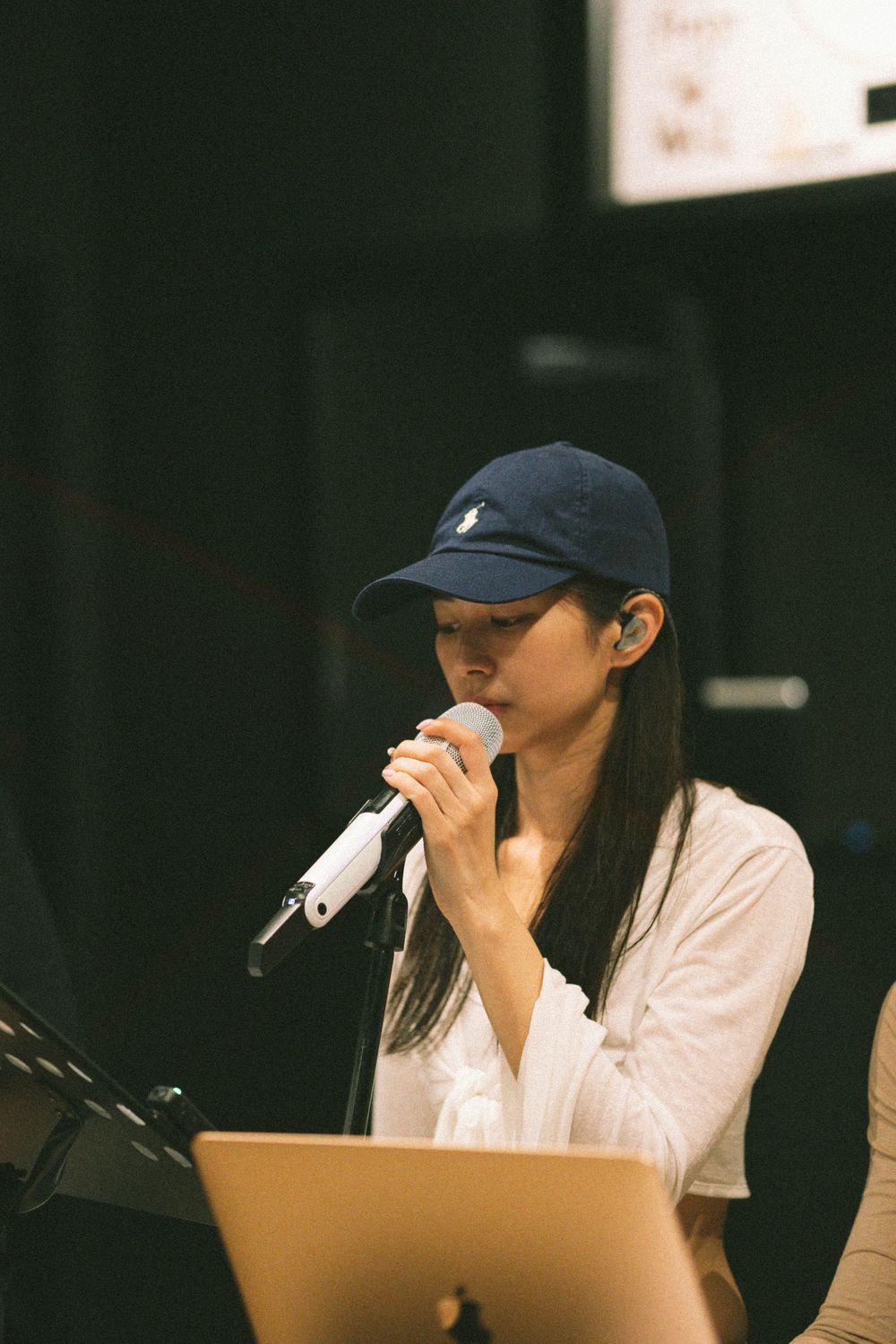 Singer in navy cap performs with microphone at music venue with laptop.