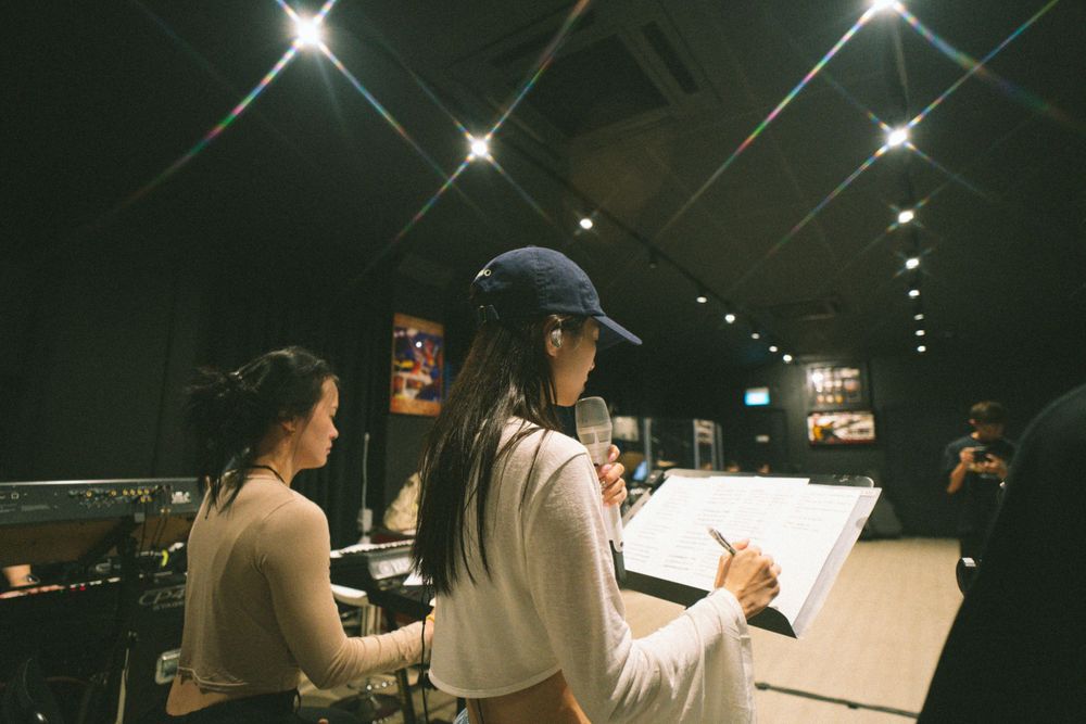 Musicians review sheet music together during a nighttime studio session.