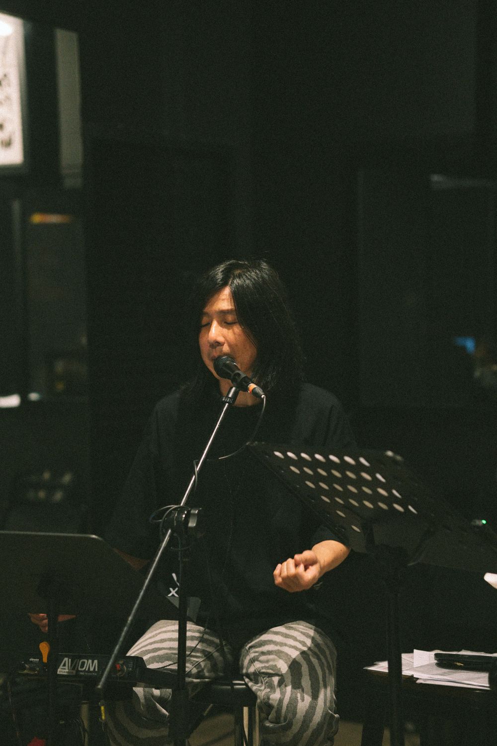 Musician in black attire performs at microphone with music stand.