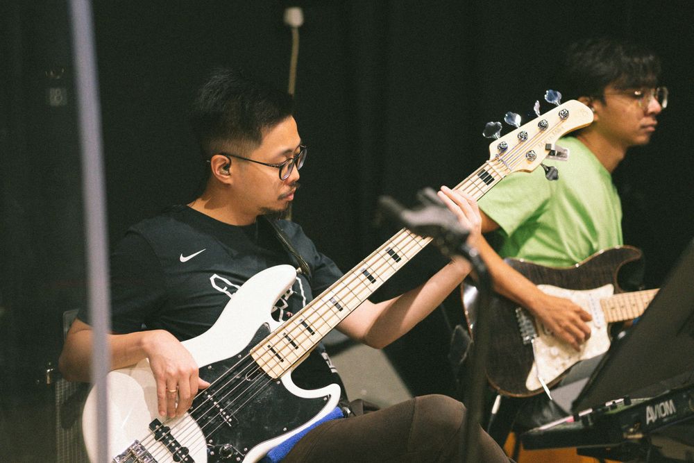 Musicians perform with electric guitars during band rehearsal in a dark studio setting.