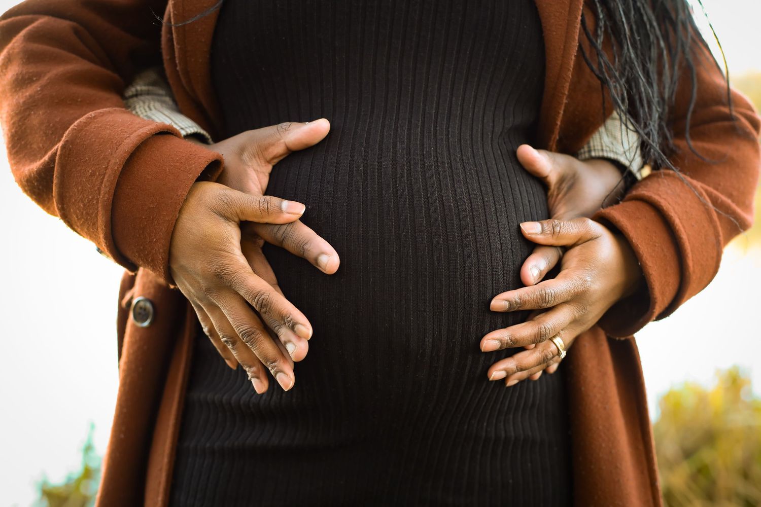Silhouette of hands tenderly framing pregnant belly in golden light.