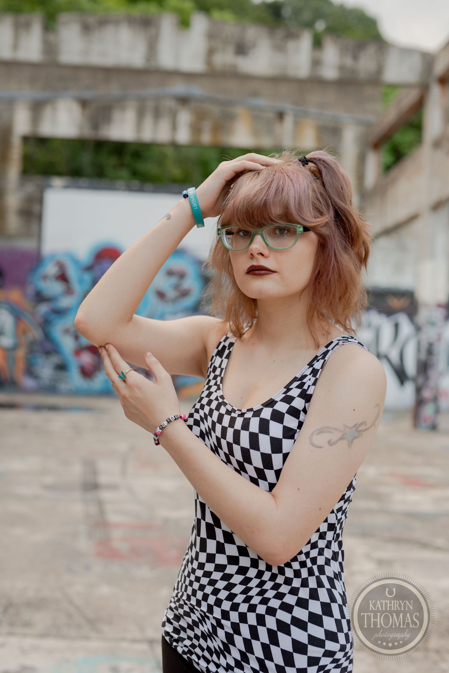 Artistic portrait with checkered tank top and glasses against urban graffiti backdrop.