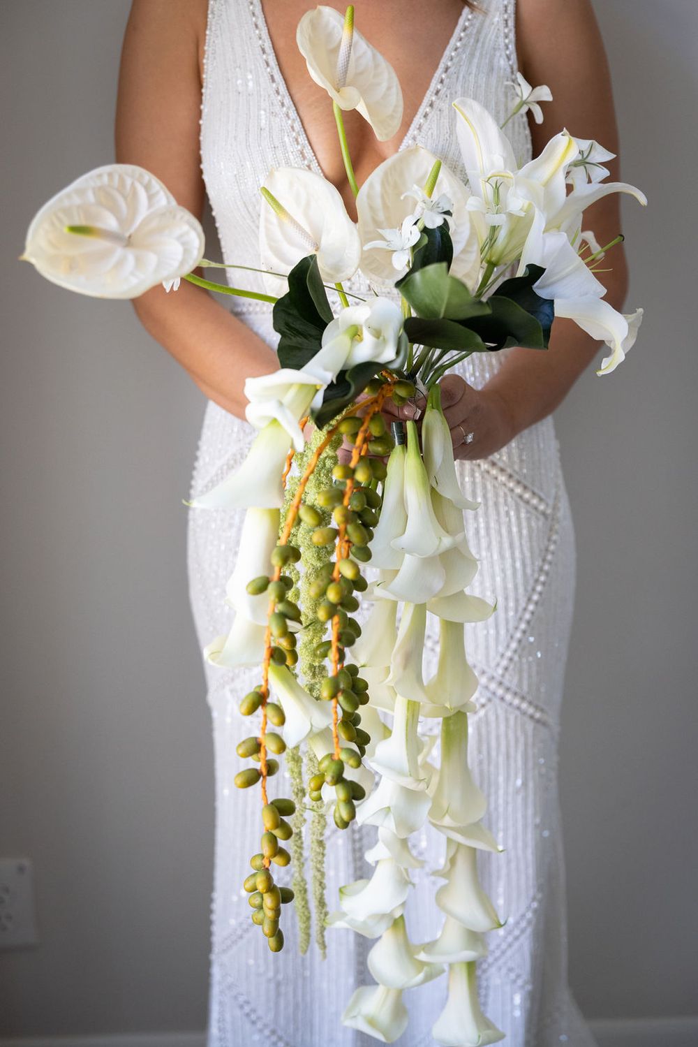 Bride holding dramatic cascading bouquet with calla lilies, orchids, and tropical greenery.