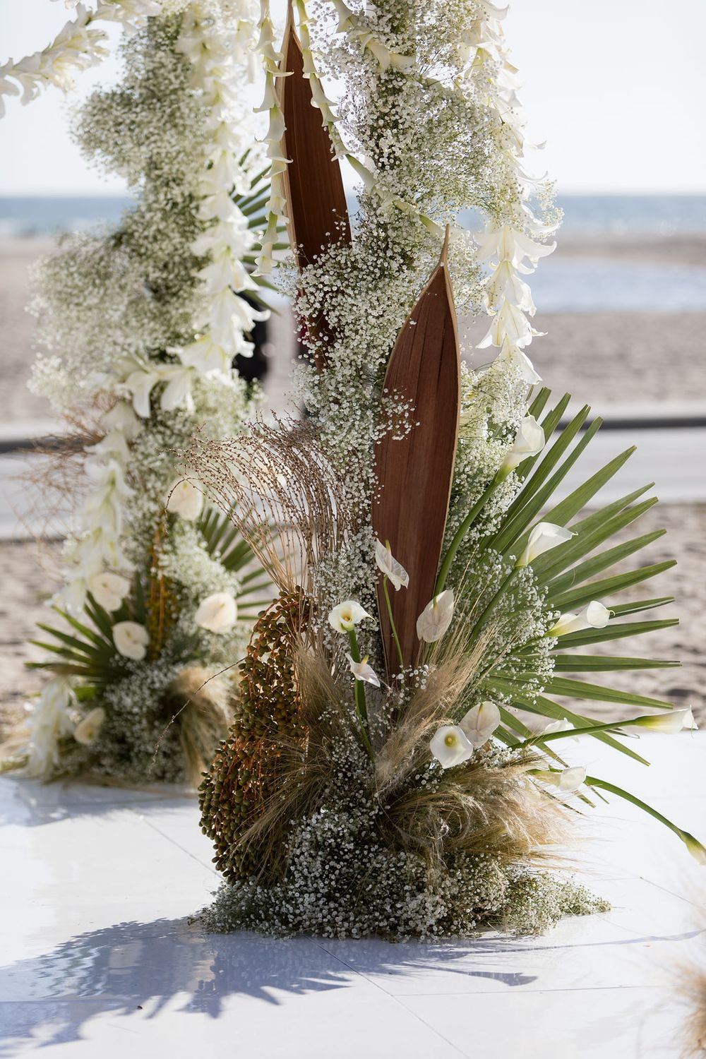 Beach wedding decor featuring dried palm fronds, white flowers, and pampas grass.