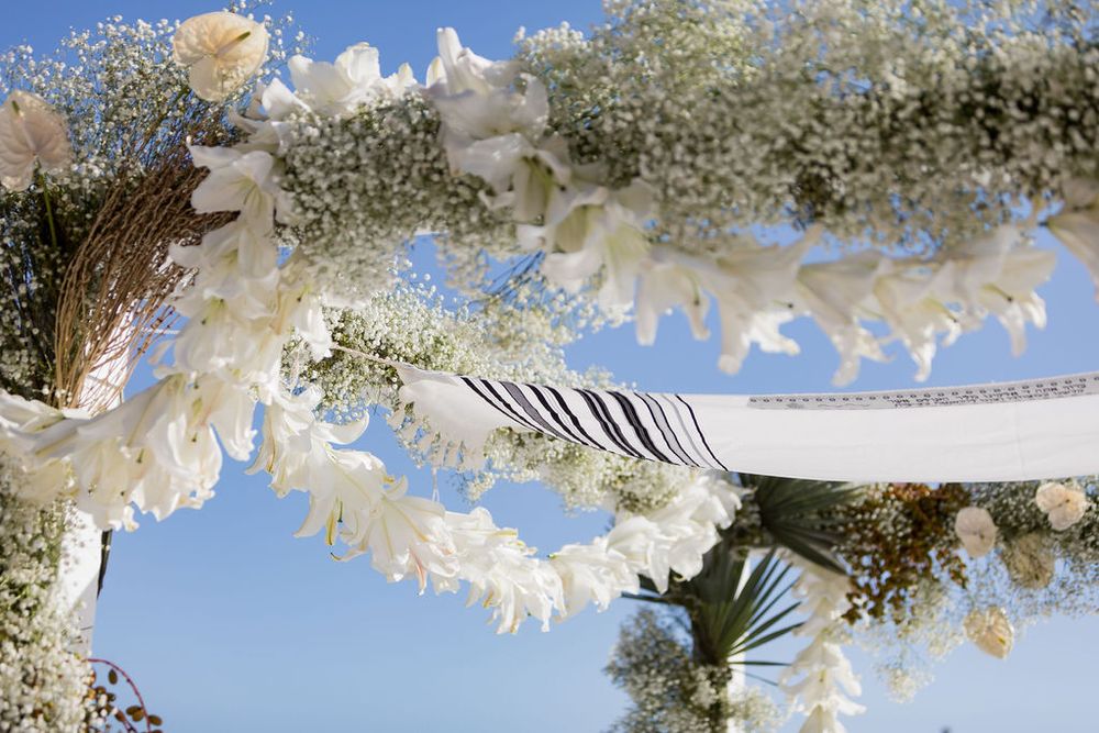 Close-up of floral arch with white flowers, baby's breath, and dried grasses against blue sky.