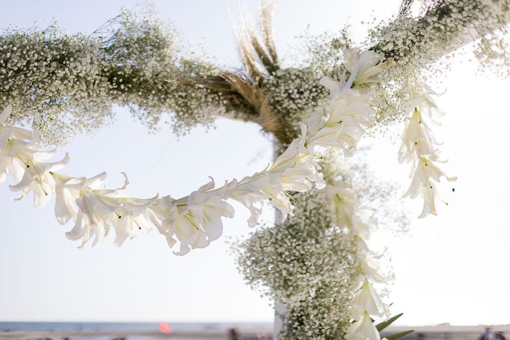 Close-up of floral garland with white flowers and baby's breath against blurred beach background.