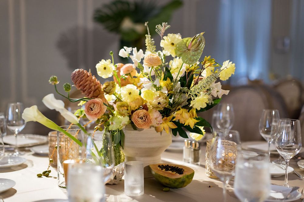 Elegant table setting with colorful floral centerpiece in yellow and peach tones.