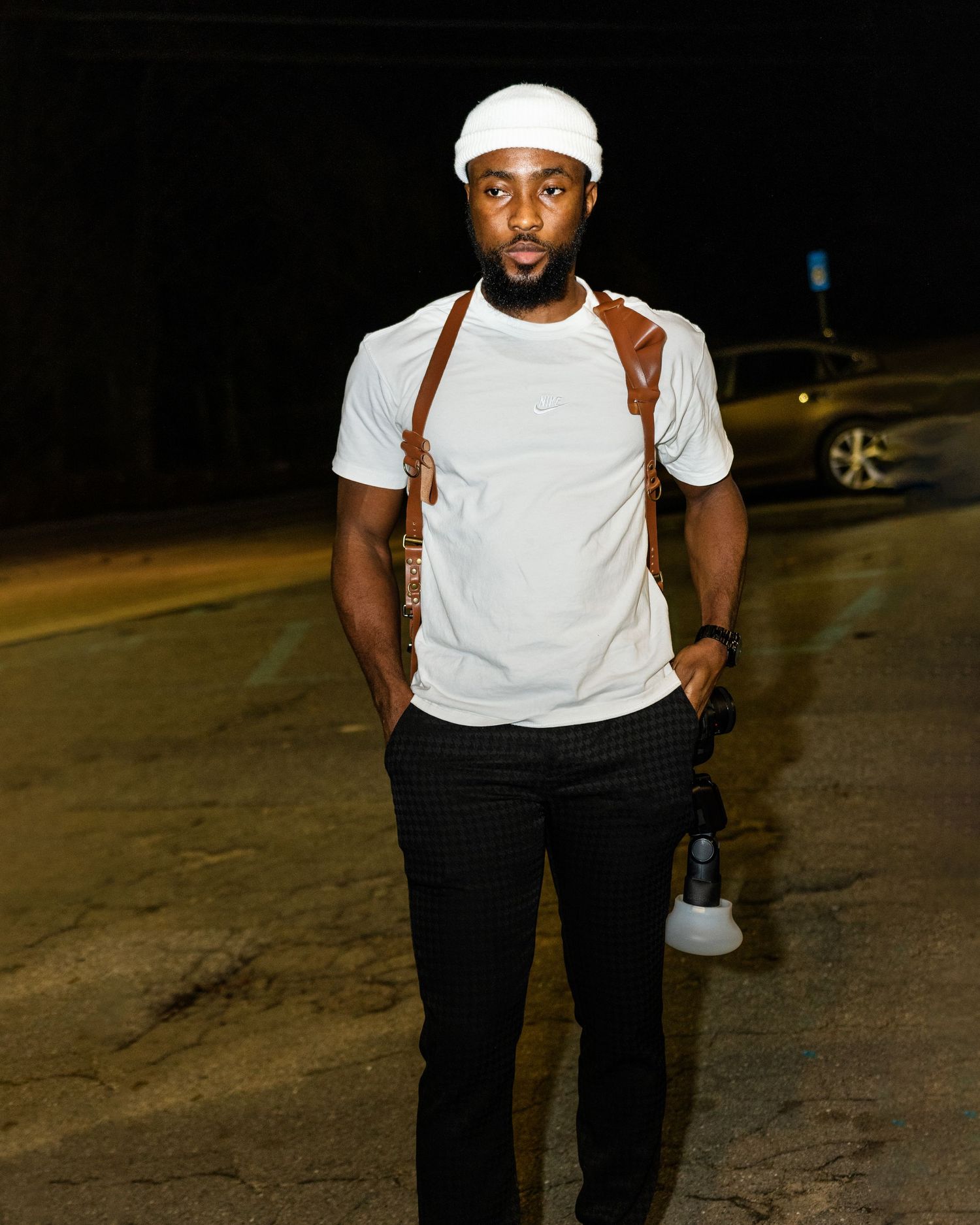 A nighttime portrait of someone wearing a white cap and t-shirt with suspenders.
