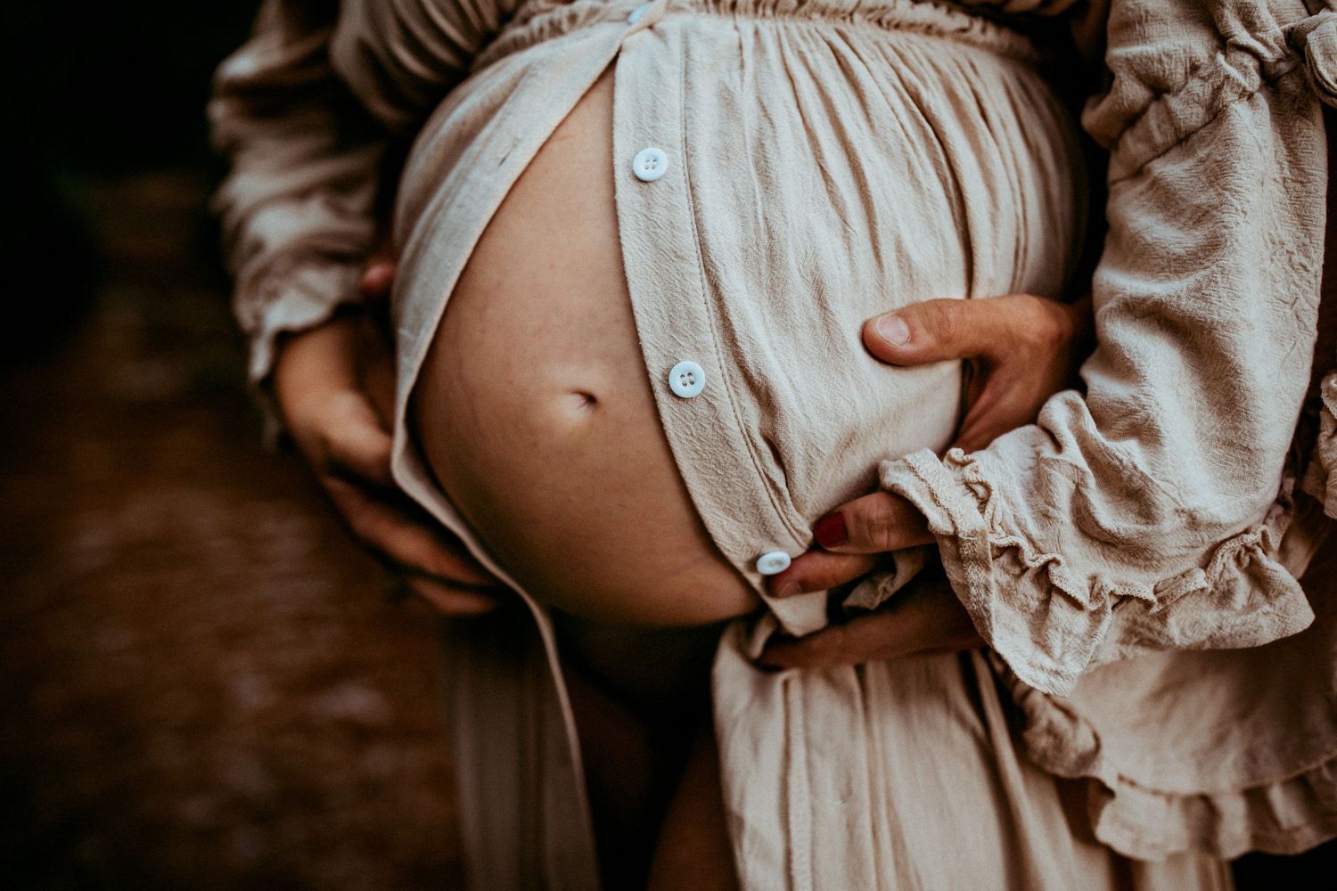 An artistic maternity photo showing a pregnant belly in a cream-colored dress.
