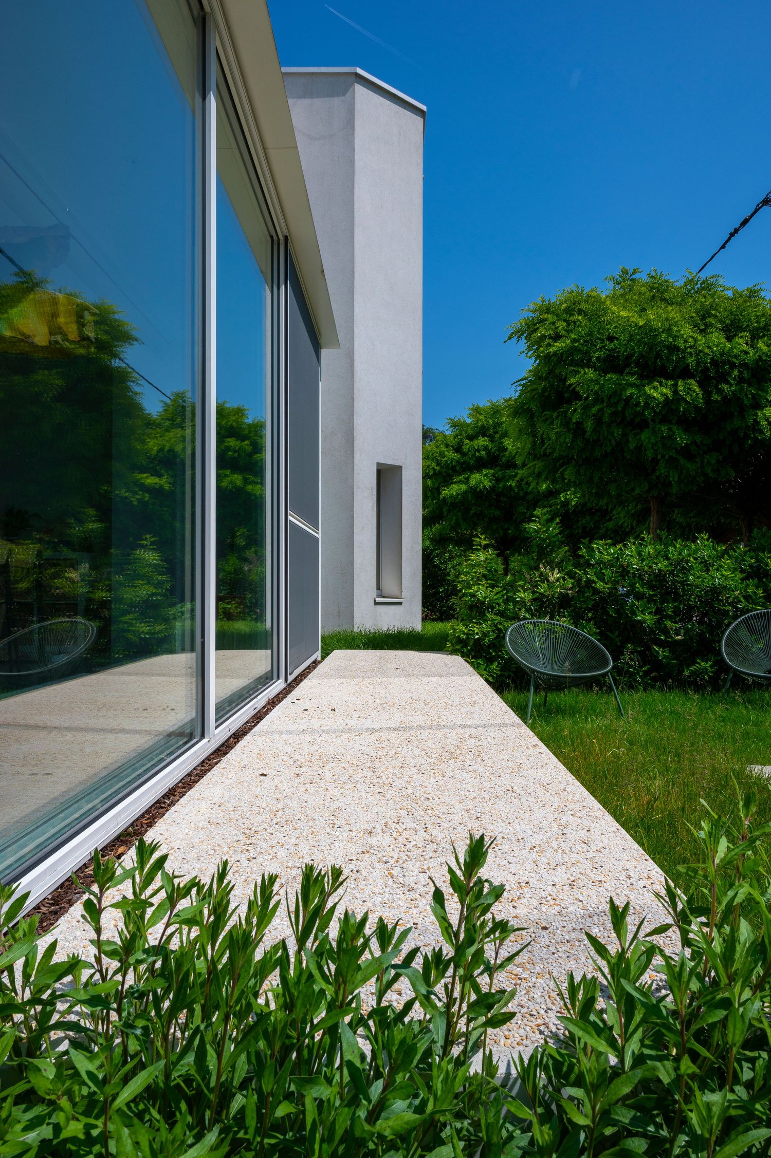 White modern building exterior with crushed stone patio and lush green landscaping.