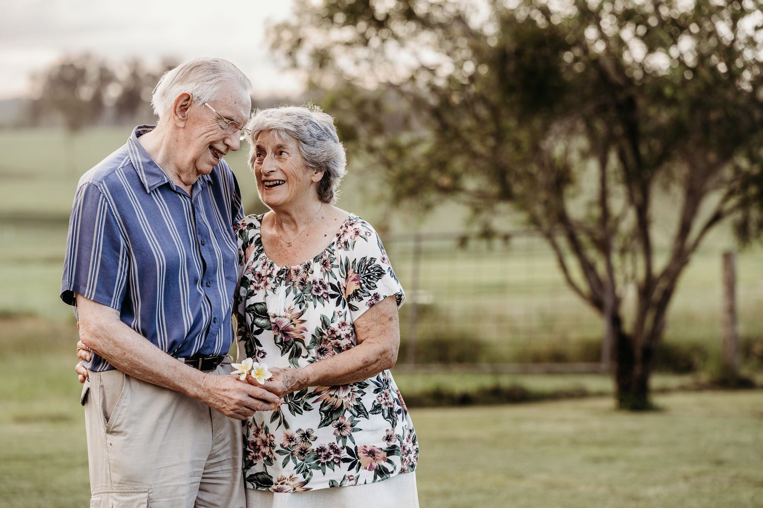 Elderly couple sharing a tender moment outdoors in casual attire.