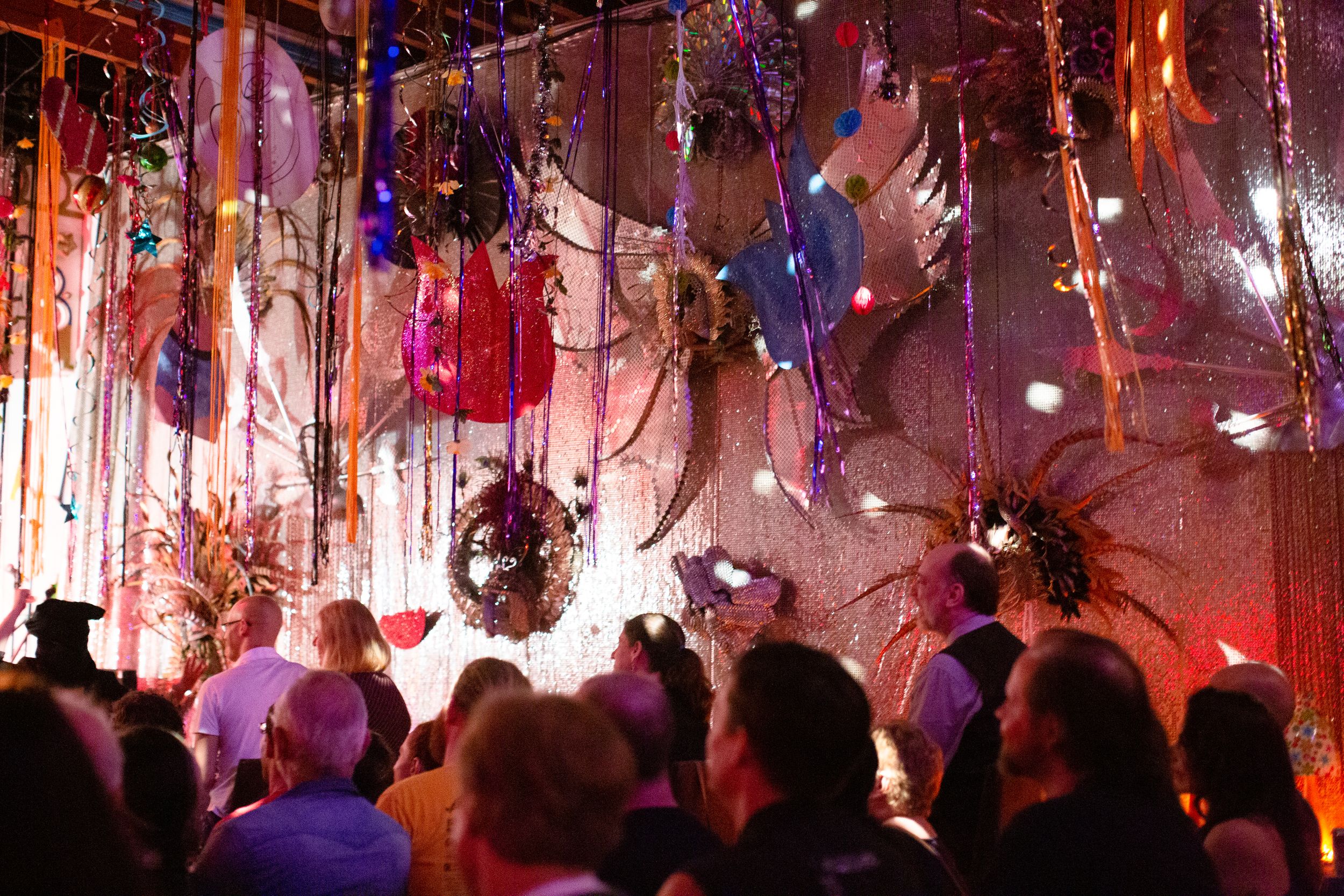 Colorful hanging decorations illuminate a crowded dance floor during a festive celebration.